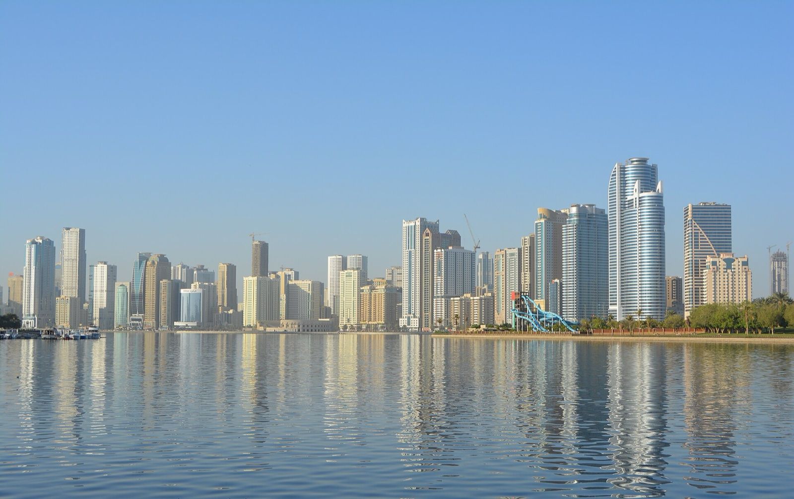 Sharjah city skyline reflected in calm lagoon water on a clear day