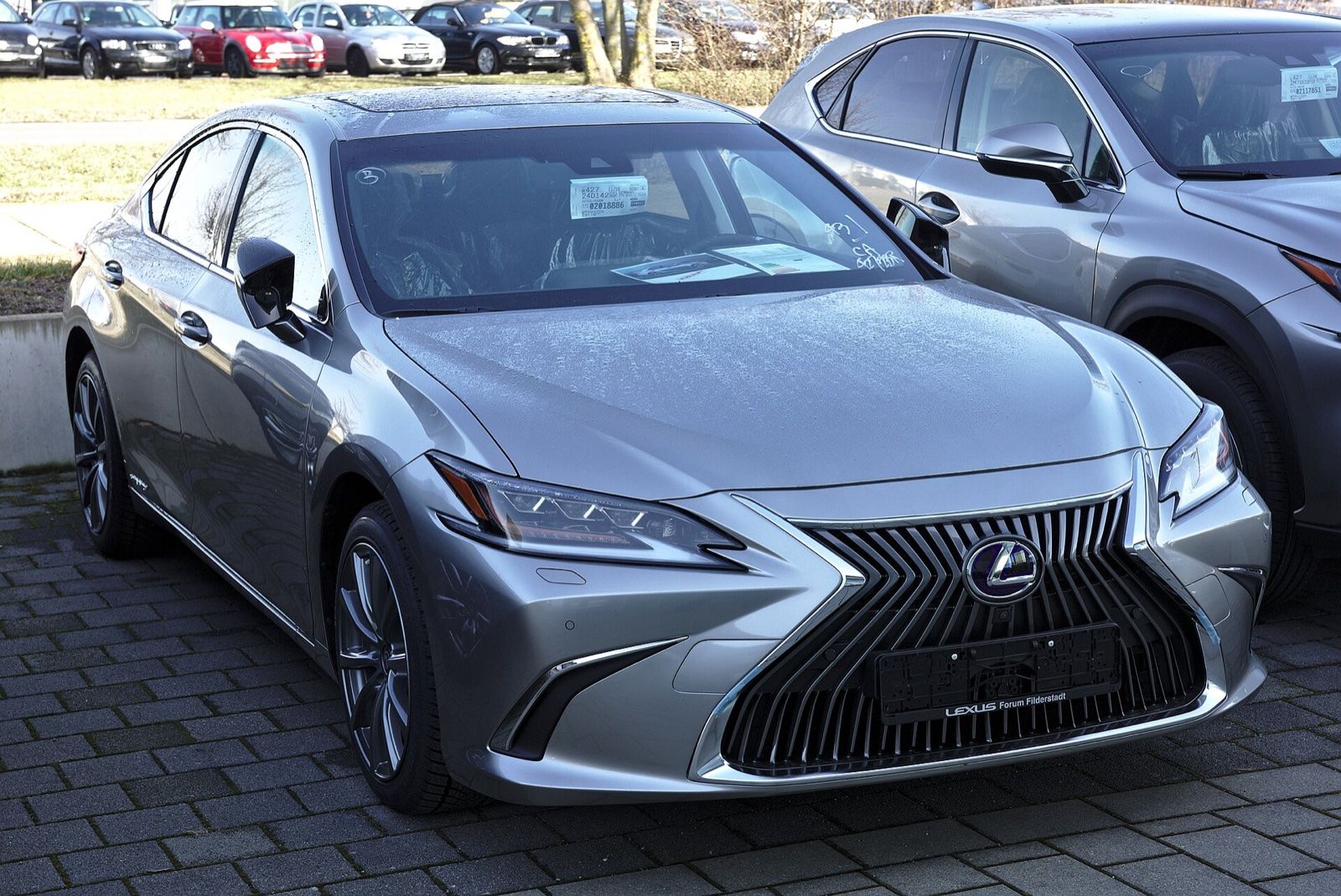 Silver Lexus ES 300h hybrid sedan, front three-quarter view, parked at a dealership
