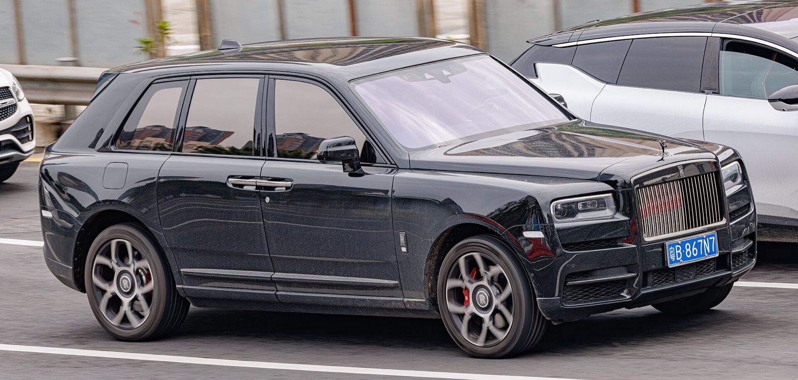 Black Rolls-Royce Cullinan SUV driving on a city road, side three-quarter view